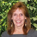 Photograph of Dr. Lynne Penberthy of the NCI standing in front of a lovely green hedge. 